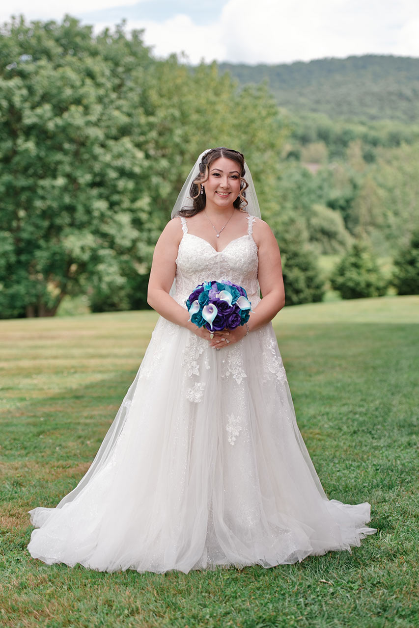 Bride in a white lace wedding gown holding a colorful bouquet during an outdoor bridal portrait in New England